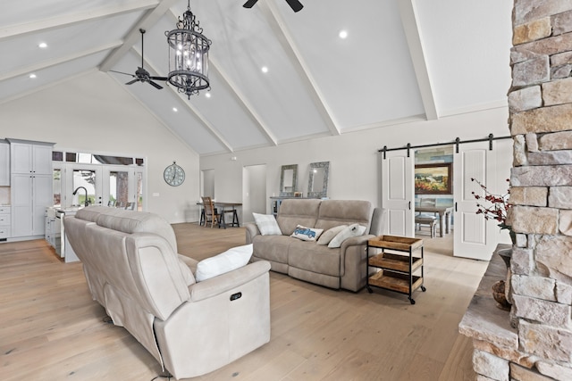 living room featuring ceiling fan with notable chandelier, a barn door, light hardwood / wood-style floors, and high vaulted ceiling