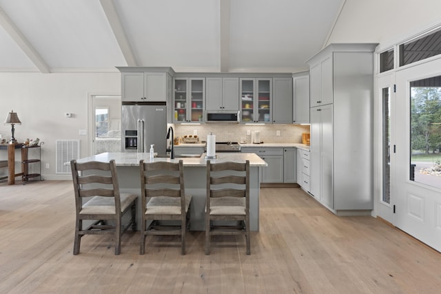 kitchen with appliances with stainless steel finishes, gray cabinetry, a breakfast bar, a kitchen island with sink, and beamed ceiling