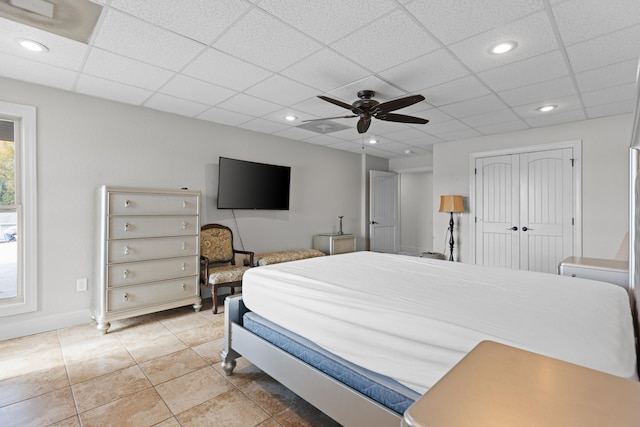 bedroom with a drop ceiling, a closet, ceiling fan, and light tile patterned flooring