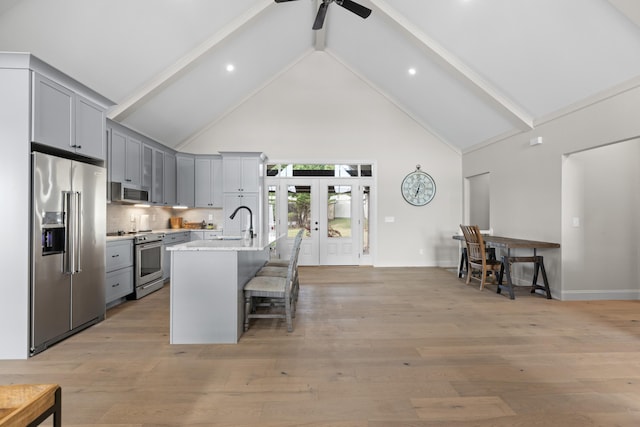 kitchen featuring stainless steel appliances, light stone counters, gray cabinets, a breakfast bar, and a center island with sink