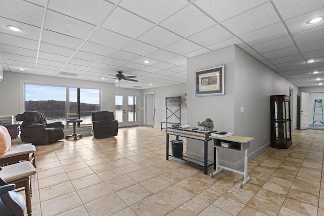 living room with ceiling fan, a drop ceiling, and french doors