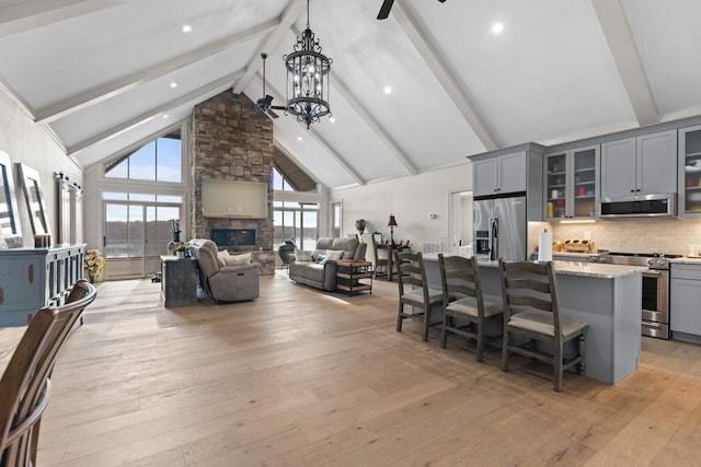 kitchen featuring gray cabinetry, a kitchen island with sink, high vaulted ceiling, appliances with stainless steel finishes, and a kitchen bar