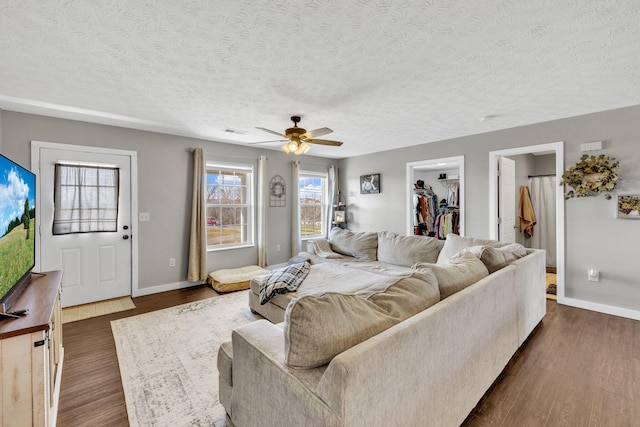 living room with a textured ceiling, dark wood-style flooring, visible vents, and baseboards