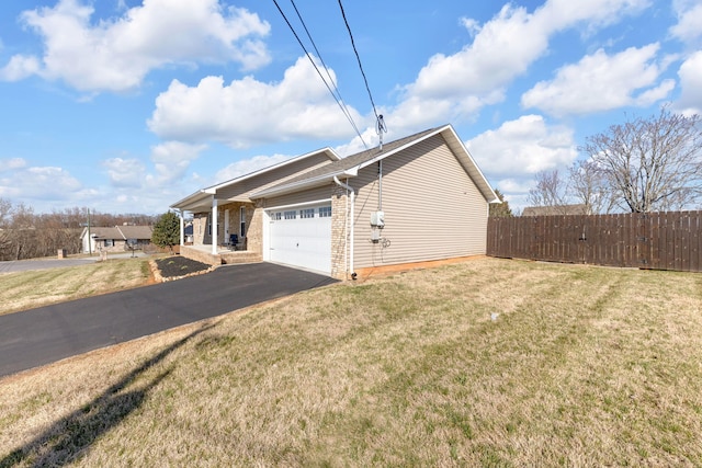 view of side of home featuring aphalt driveway, an attached garage, fence, a yard, and brick siding