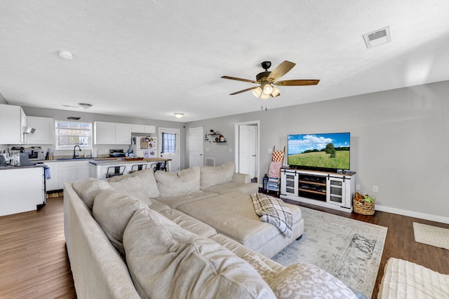 living area with a textured ceiling, ceiling fan, wood finished floors, visible vents, and baseboards