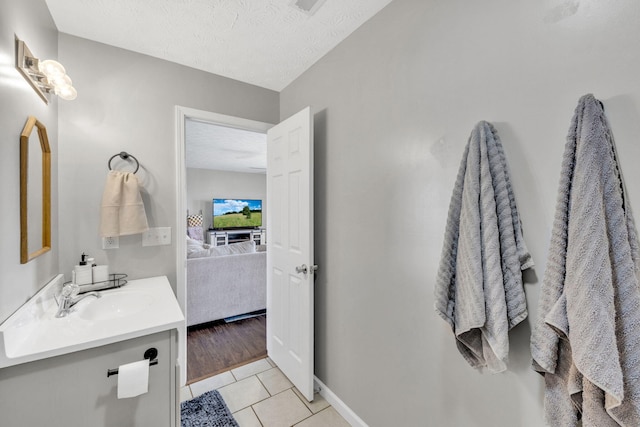 ensuite bathroom featuring a textured ceiling, tile patterned flooring, connected bathroom, vanity, and baseboards