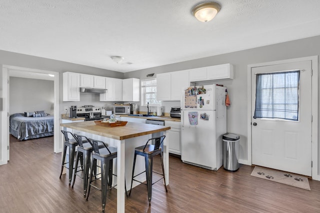 kitchen featuring white appliances, a breakfast bar area, wood counters, and white cabinetry