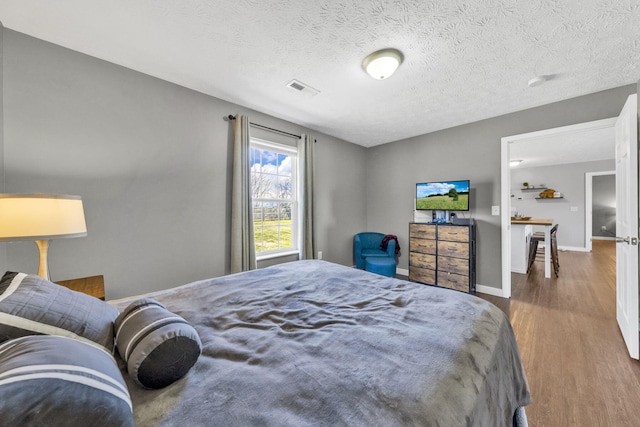 bedroom with visible vents, a textured ceiling, baseboards, and wood finished floors