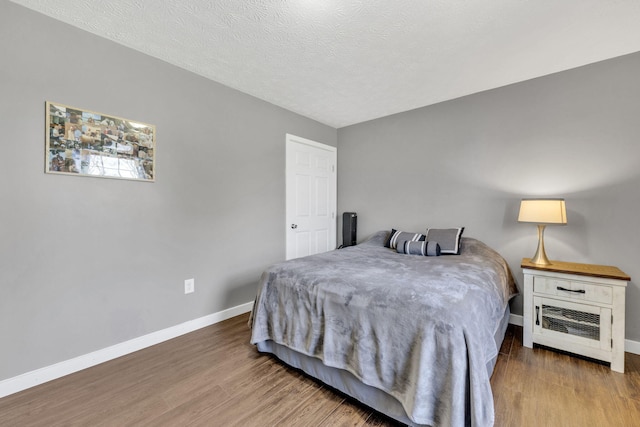 bedroom featuring a textured ceiling, wood finished floors, and baseboards