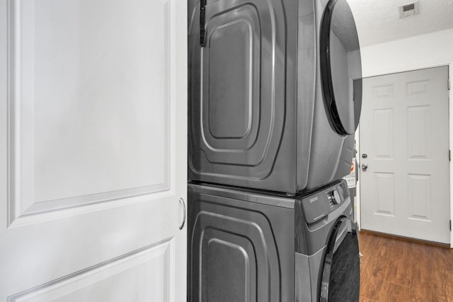 laundry room featuring laundry area, visible vents, dark wood finished floors, stacked washer / dryer, and a textured ceiling