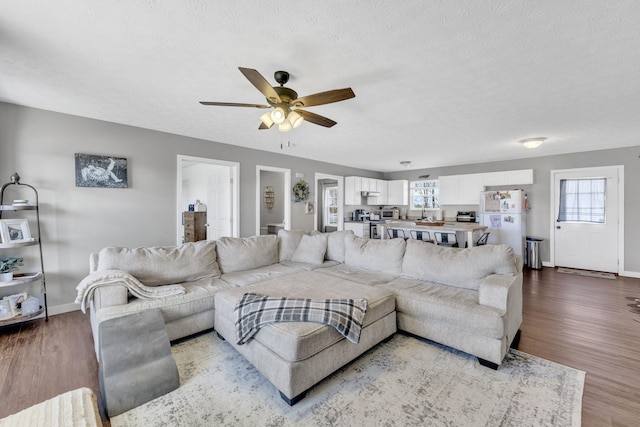 living room featuring a textured ceiling, wood finished floors, a ceiling fan, and baseboards