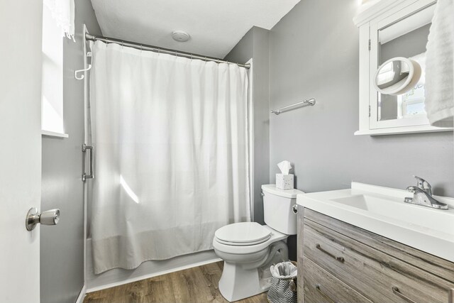full bath featuring wood finished floors, shower / bath combo with shower curtain, toilet, and vanity