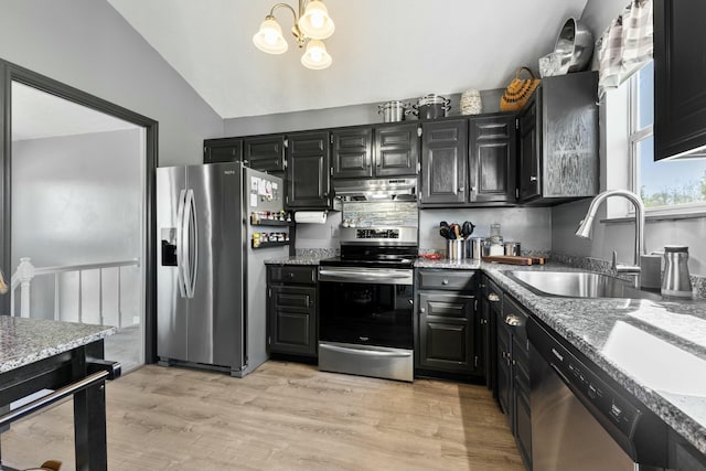 kitchen with a sink, vaulted ceiling, dark cabinetry, under cabinet range hood, and appliances with stainless steel finishes