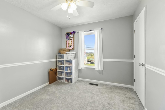 carpeted empty room with a textured ceiling, a ceiling fan, baseboards, and visible vents