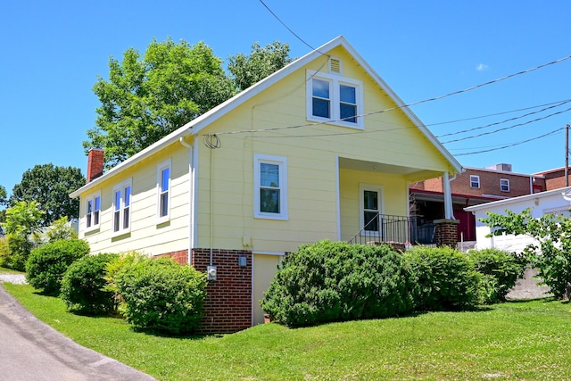 exterior space with brick siding, a front lawn, a chimney, and a porch