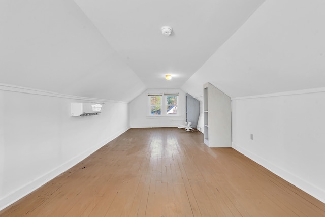 bonus room with wood-type flooring, baseboards, a wall mounted AC, and lofted ceiling