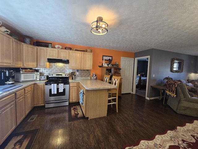 kitchen featuring dark wood-style floors, white microwave, a peninsula, stainless steel electric range, and under cabinet range hood