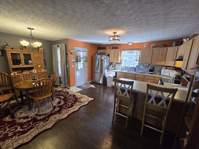 kitchen featuring dark wood finished floors, a peninsula, freestanding refrigerator, under cabinet range hood, and a chandelier