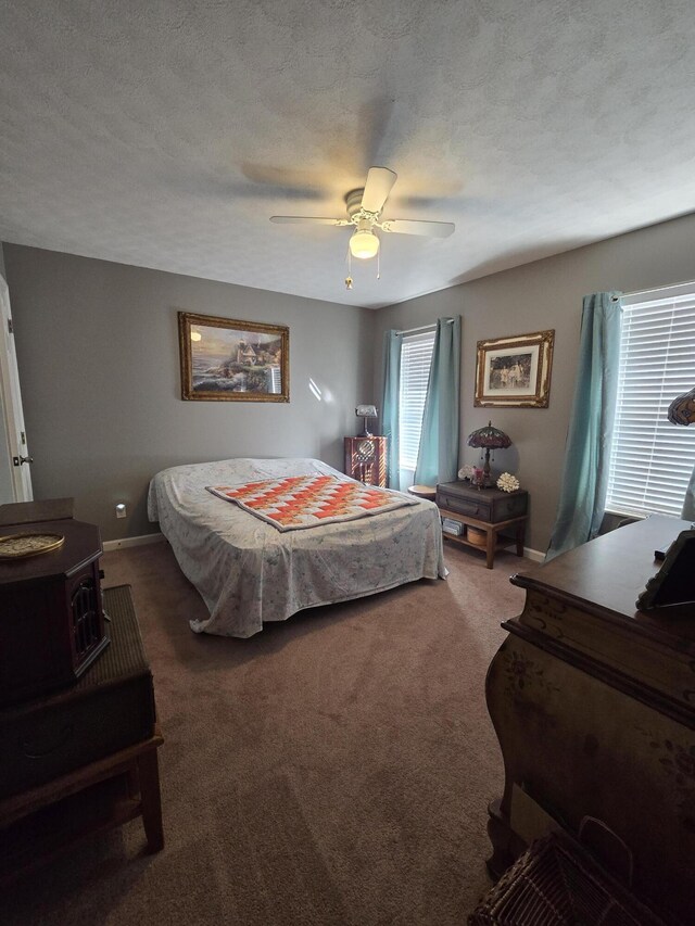 carpeted bedroom featuring baseboards, a textured ceiling, ceiling fan, and a wood stove