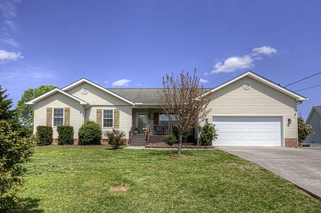 single story home with a porch, driveway, a front lawn, and an attached garage