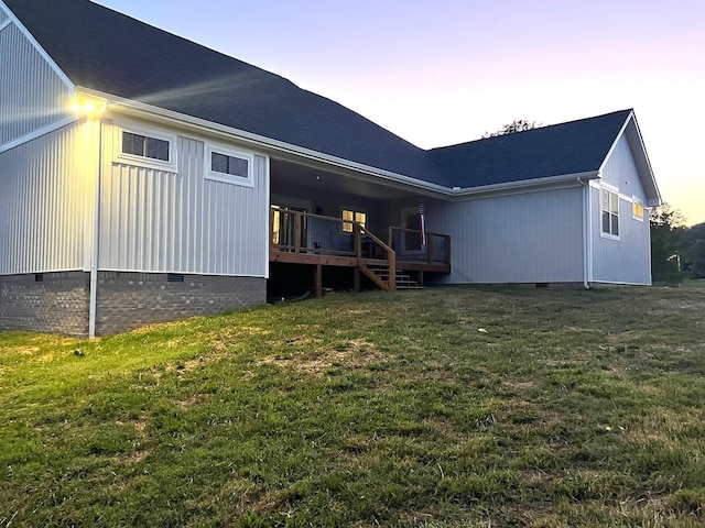 back house at dusk featuring a deck and a lawn