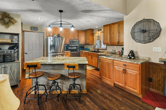 kitchen featuring a center island, stainless steel appliances, decorative light fixtures, a textured ceiling, and a breakfast bar area