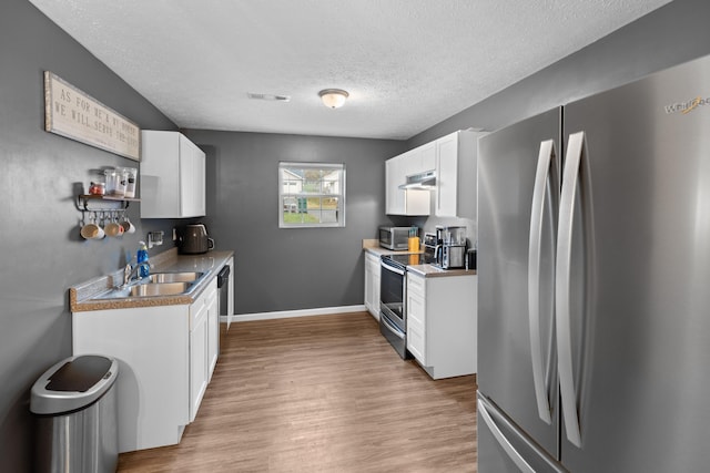 kitchen featuring light wood-type flooring, a textured ceiling, stainless steel appliances, and white cabinetry