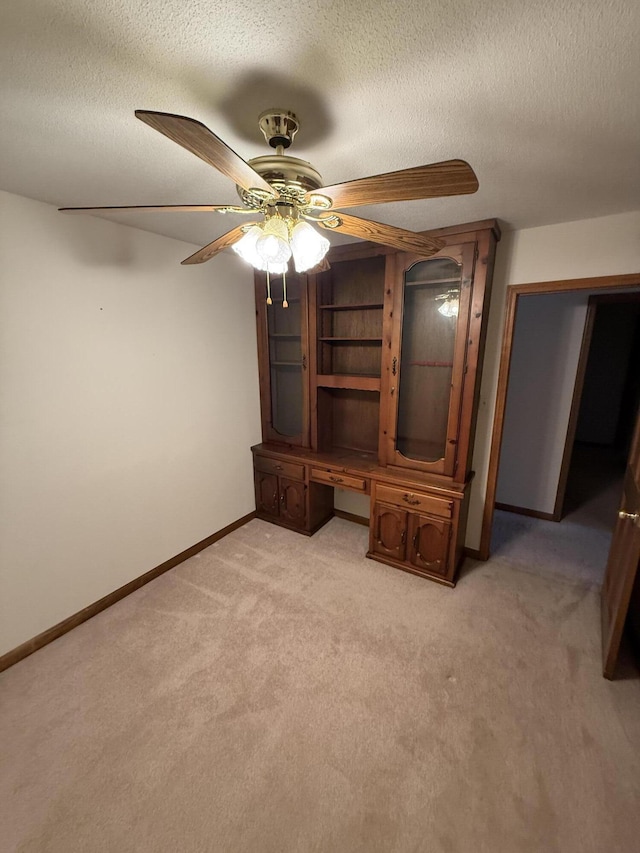 interior space with built in desk, light colored carpet, a textured ceiling, and baseboards