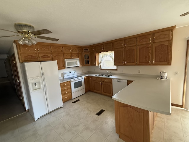 kitchen featuring brown cabinets, light countertops, a sink, white appliances, and a peninsula