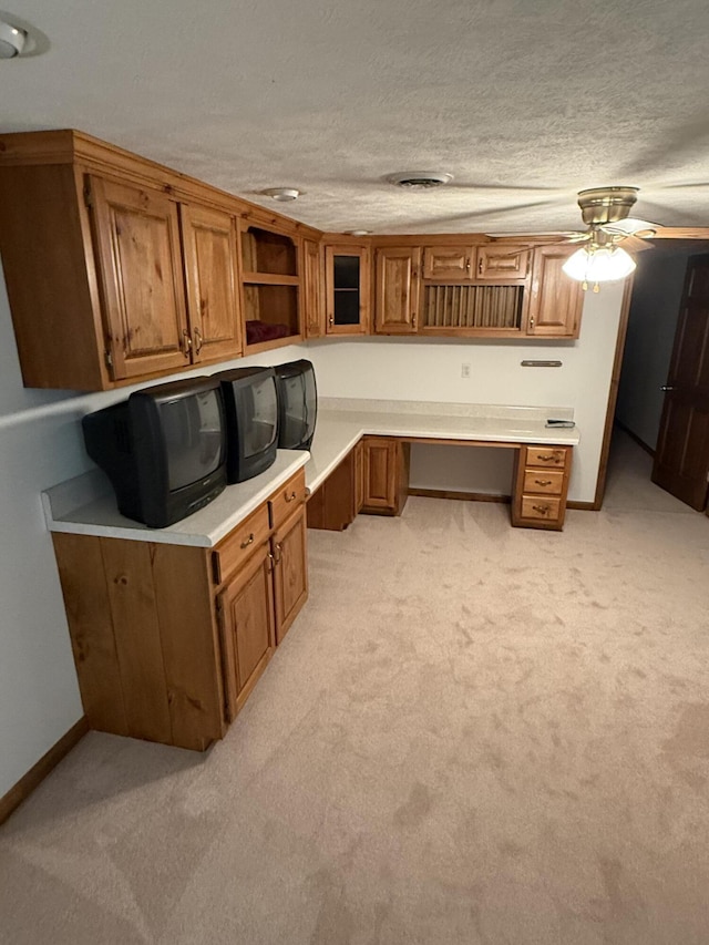 unfurnished office with light carpet, a textured ceiling, baseboards, and built in desk