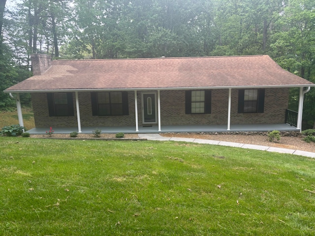 view of front of home with a front lawn, covered porch, roof with shingles, a chimney, and brick siding