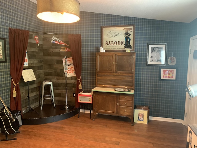 interior space featuring wallpapered walls, lofted ceiling, and wood finished floors