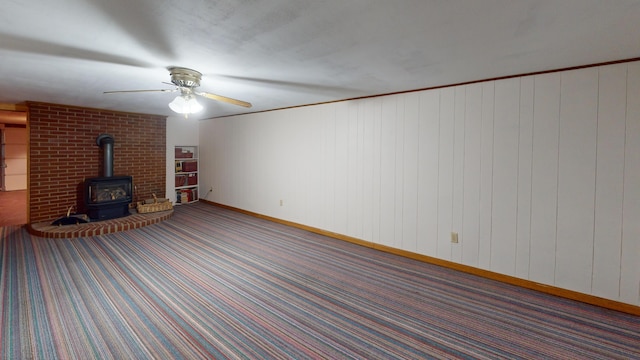 unfurnished living room featuring a wood stove, crown molding, wooden walls, and carpet floors