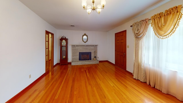 unfurnished living room featuring a stone fireplace, a notable chandelier, and hardwood / wood-style flooring