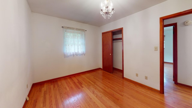 unfurnished bedroom with a notable chandelier, light wood-type flooring, and a closet