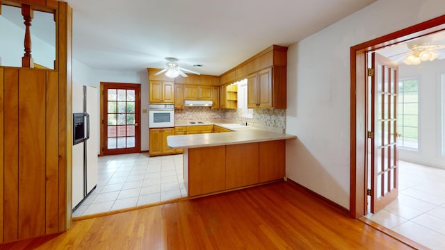 kitchen featuring decorative backsplash, white appliances, light hardwood / wood-style flooring, and a healthy amount of sunlight