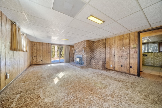 unfurnished living room featuring a brick fireplace, carpet floors, a paneled ceiling, and wood walls