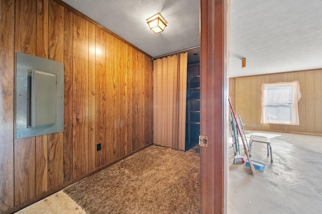 corridor with carpet flooring, electric panel, a textured ceiling, and wood walls