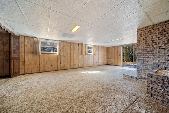 basement with wooden walls, a paneled ceiling, and carpet flooring