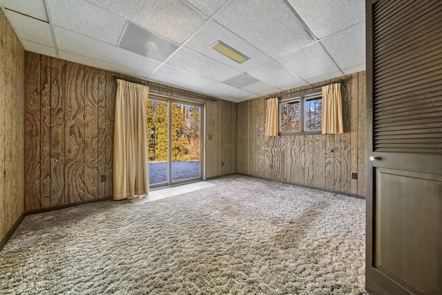 carpeted spare room featuring a paneled ceiling and wood walls