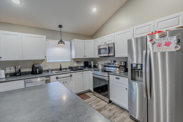 kitchen featuring sink, pendant lighting, lofted ceiling, white cabinets, and appliances with stainless steel finishes