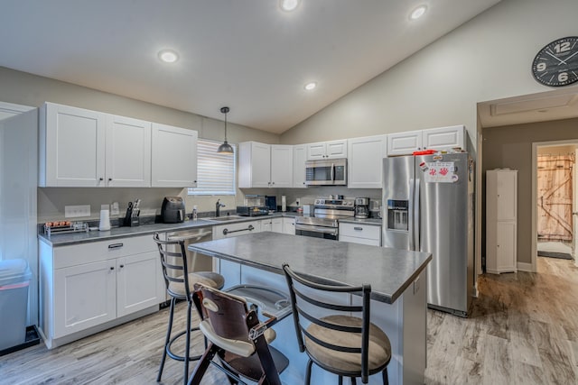 kitchen with a breakfast bar, stainless steel appliances, sink, pendant lighting, and light hardwood / wood-style floors