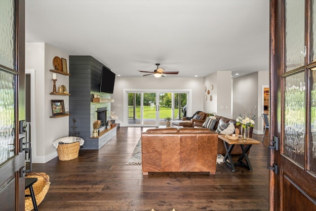 living room with ceiling fan, a large fireplace, and dark wood-type flooring