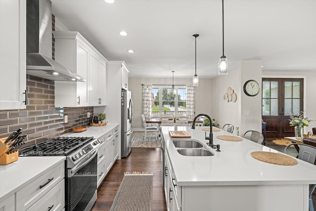 kitchen featuring stainless steel appliances, a kitchen island with sink, sink, wall chimney range hood, and decorative light fixtures