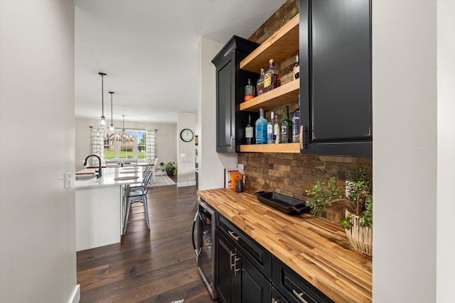 bar with sink, dark wood-type flooring, beverage cooler, hanging light fixtures, and wood counters