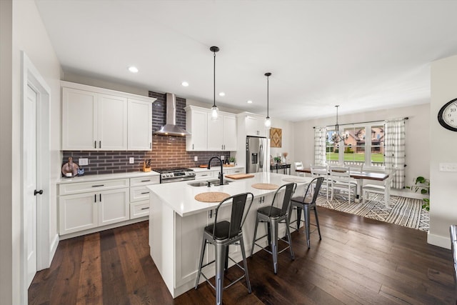 kitchen with appliances with stainless steel finishes, wall chimney exhaust hood, sink, decorative light fixtures, and white cabinets