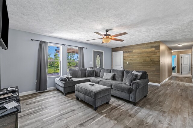living room with wood walls, wood finished floors, baseboards, ceiling fan, and a textured ceiling