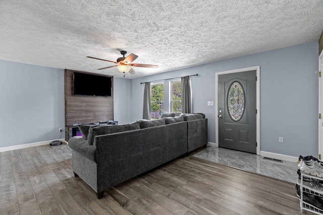 living area featuring a ceiling fan, a textured ceiling, visible vents, wood finished floors, and baseboards