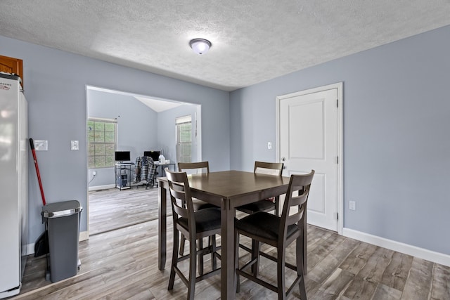 dining space with baseboards, a textured ceiling, and wood finished floors