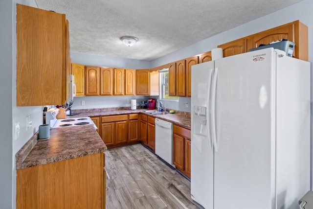 kitchen with white appliances, a textured ceiling, a sink, and light wood-style flooring